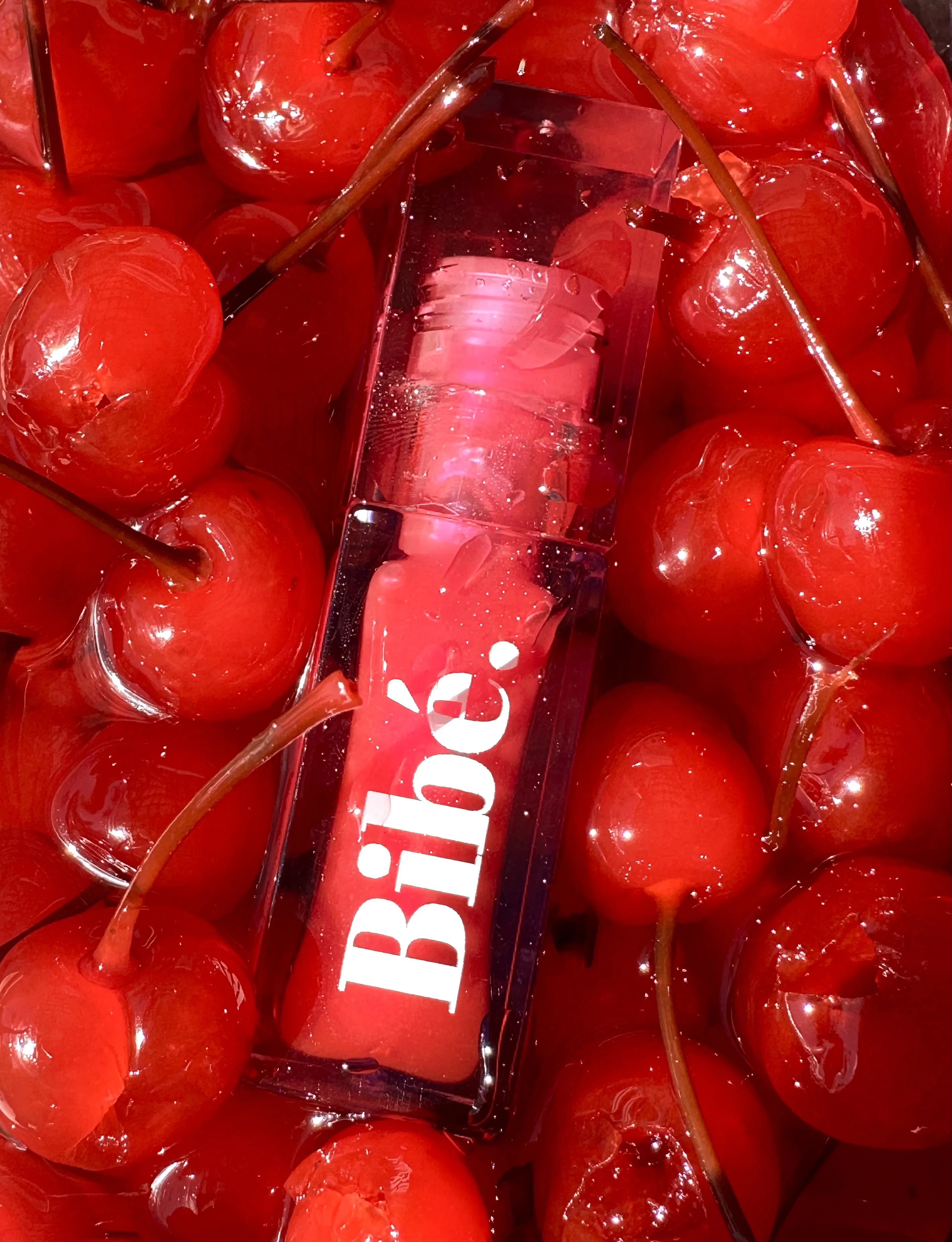 Bibé lip gloss nestled among glossy maraschino cherries