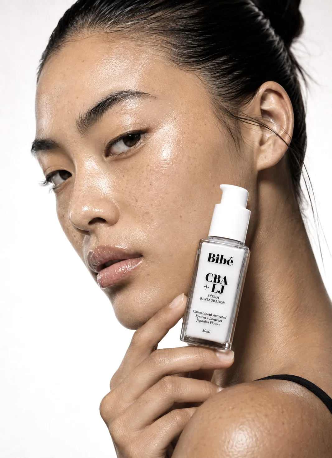 Model with hair in a bun holding a Bibé CBA + LJ bottle near her ear