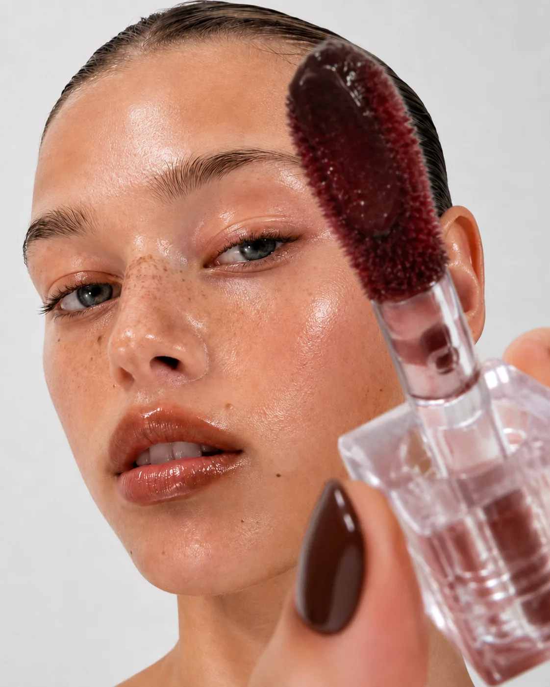 Model applying Bibé lip gloss with the wand, dewy skin close-up