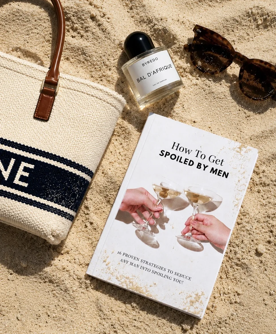 Lucky Girl Syndrome flat lay: beach tote, Byredo perfume, sunglasses and the 'How To Get Spoiled By Men' book in the sand