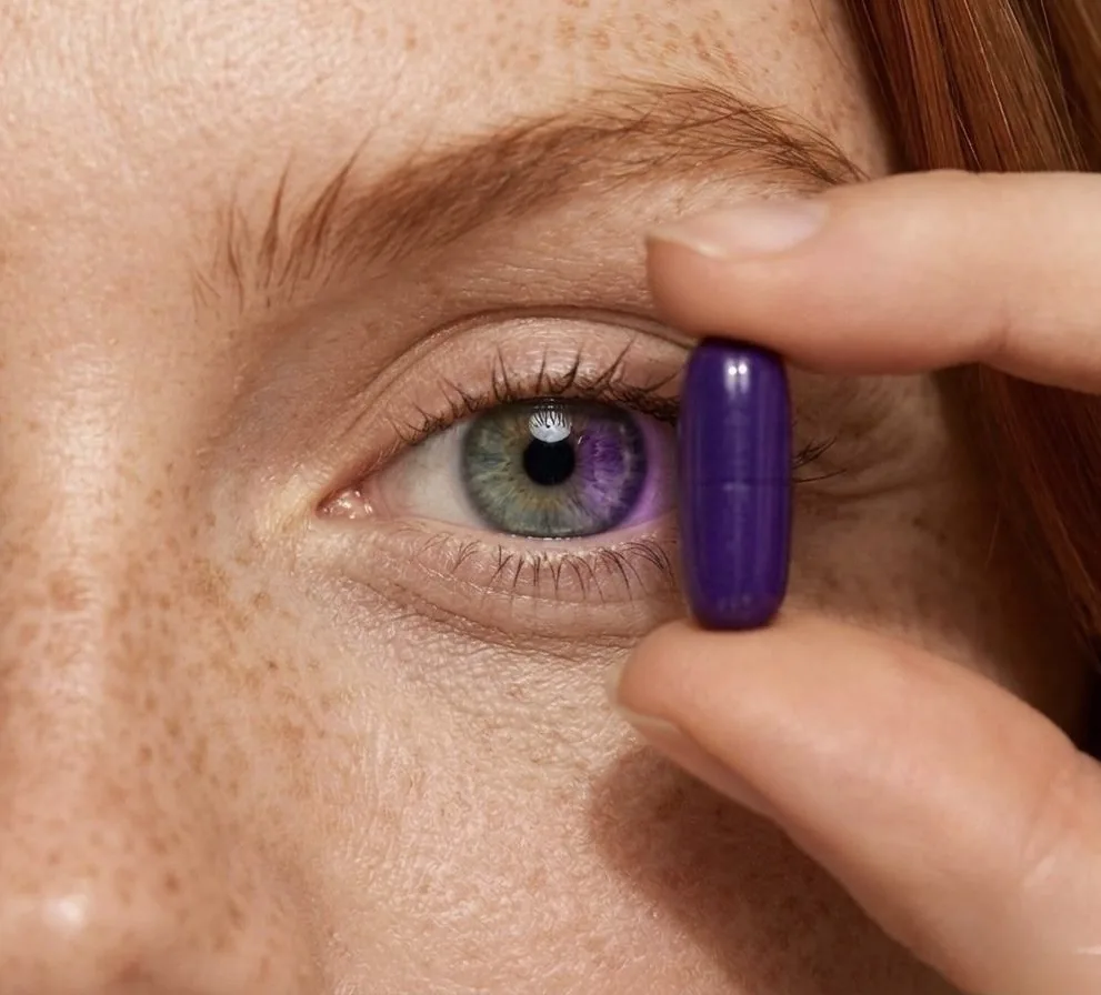 Extreme close-up of an eye with a purple Puraliv capsule held beside it